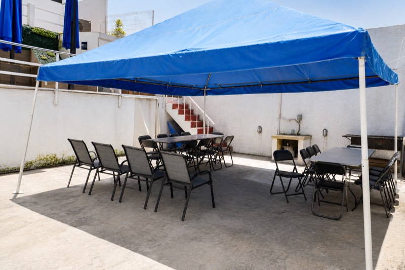 Patio techado montado para un evento, con carpa azul, mesas y sillas