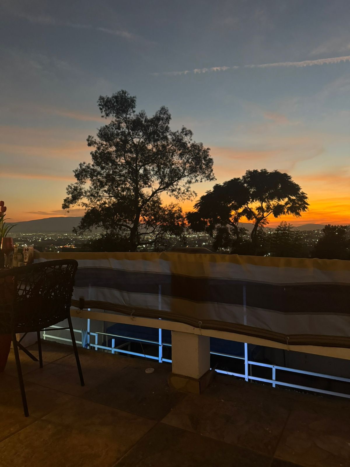 Atardecer desde la terraza: cielo naranja, árboles y las luces de la ciudad